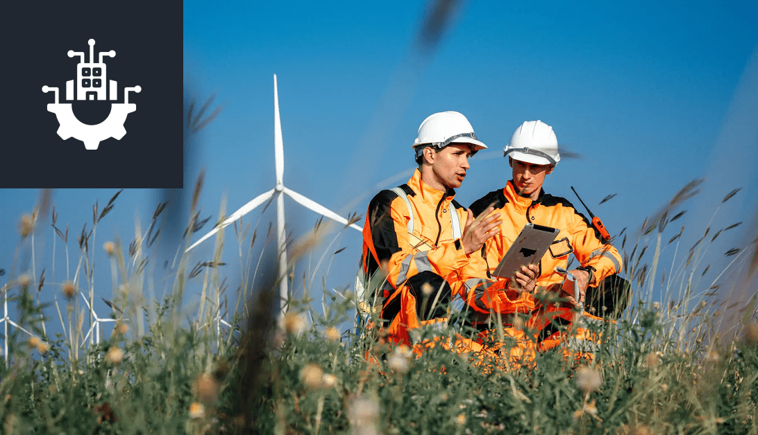 Two engineers in safety gear discuss near a wind turbine.