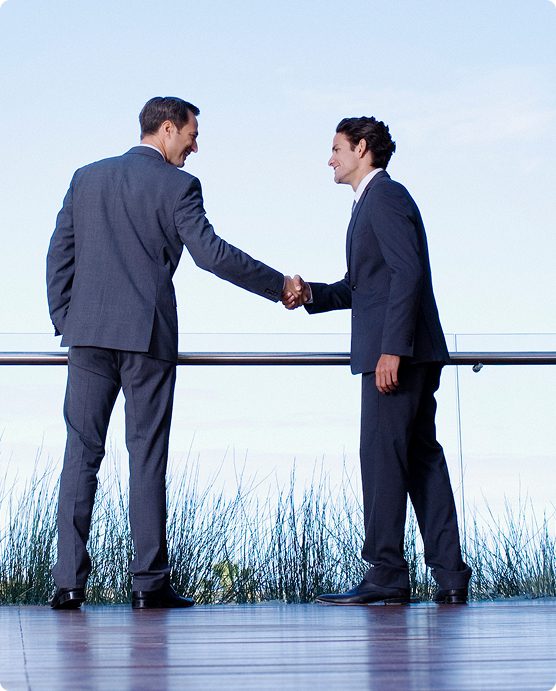 Two businessmen shaking hands outdoors by the water.