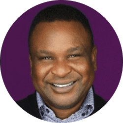 Smiling man in a patterned shirt with a purple background.