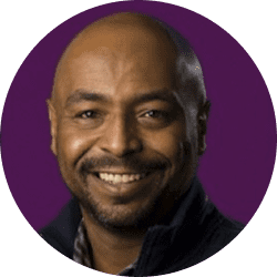 Portrait of a smiling man with a beard against a purple background.